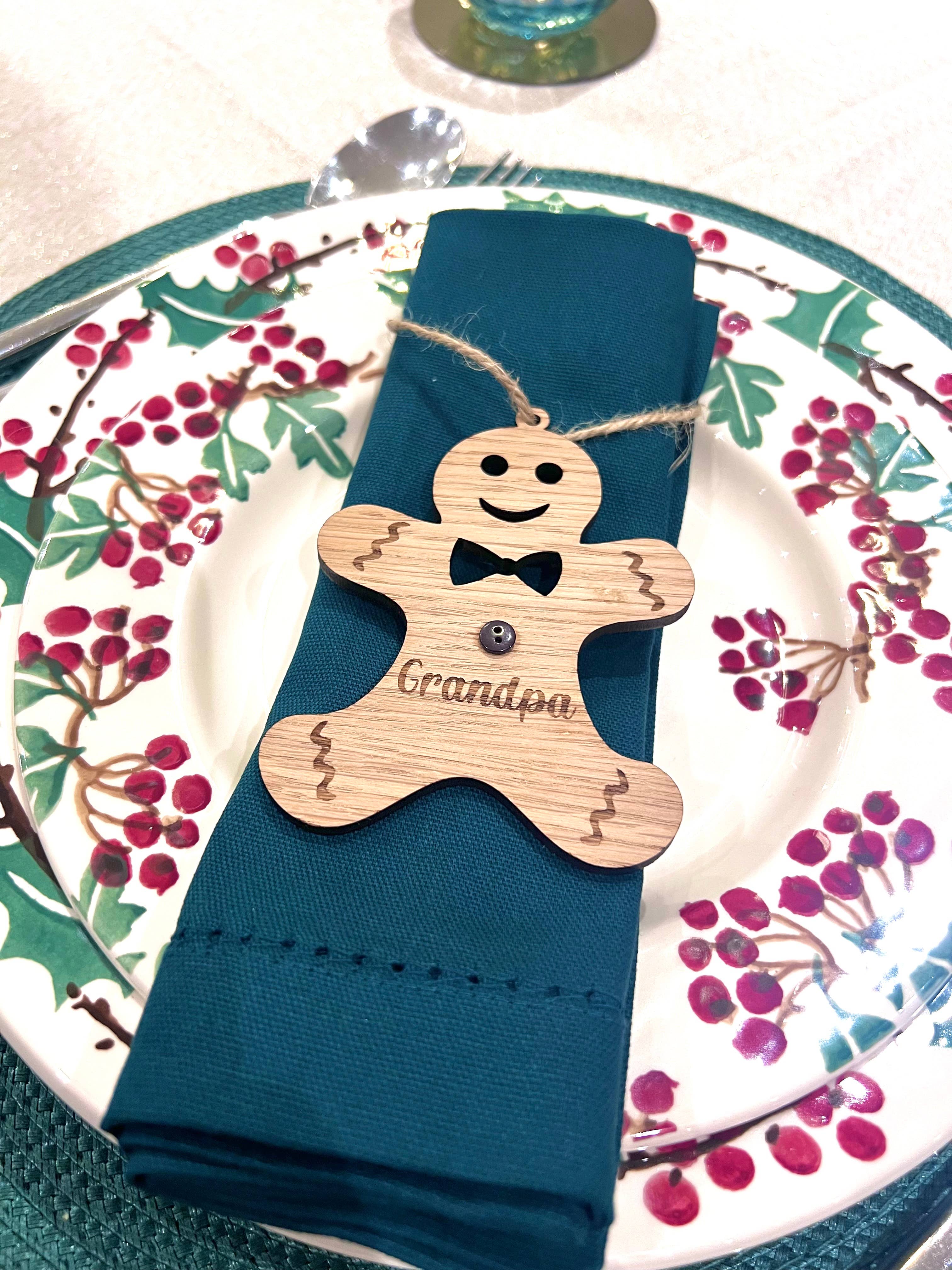 Napkin holder shaped like a gingerbread man with 'Grandpa' engraved, on a blue napkin with a decorative plate in the background.